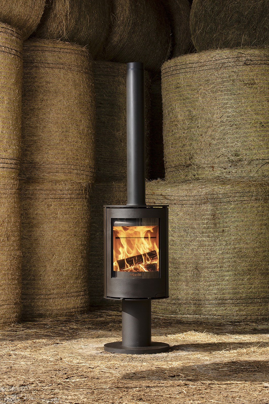 Atlantic Horizon wood-burning stove with visible flames, surrounded by stacked hay bales in a rustic outdoor setting.